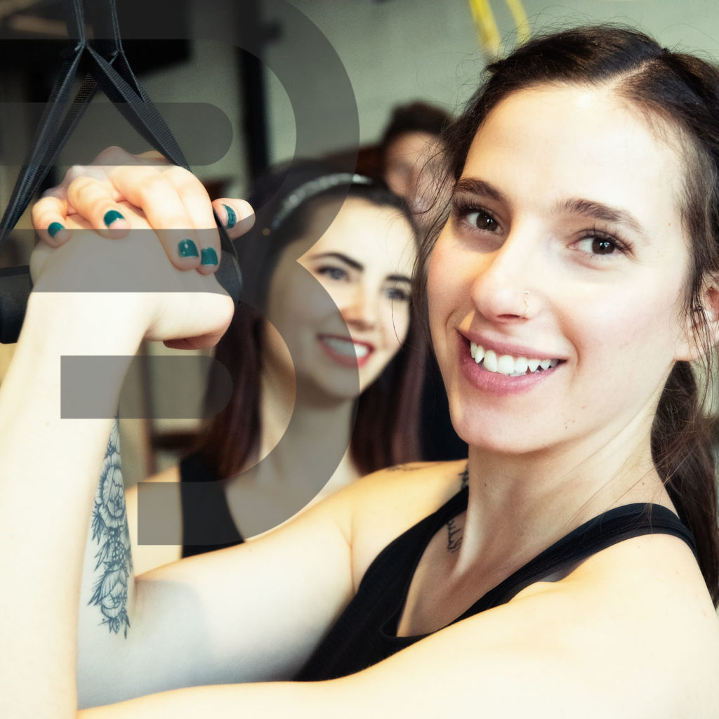 smiling women closing hands together in front of her as she flexes at the gym