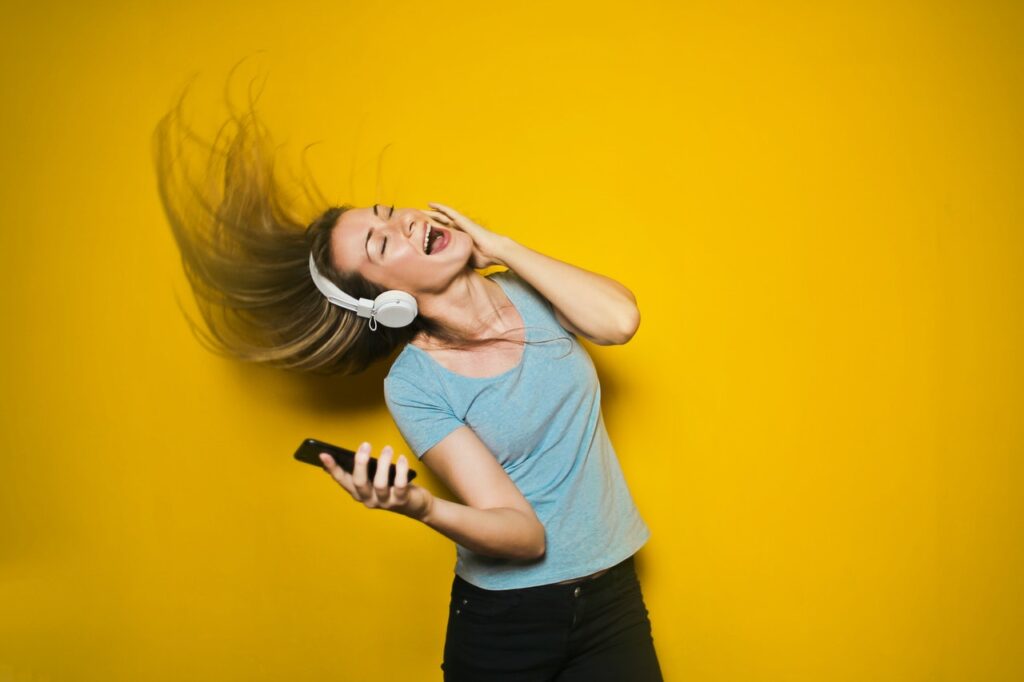woman dancing with white headphones and cellphone on yellow background