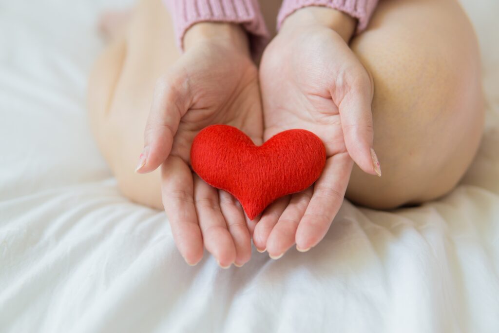 person kneeling on bed holding red cloth heart in hands